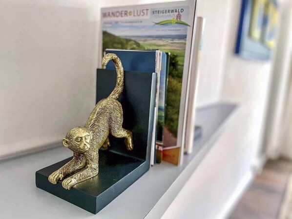 A gold monkey figurine on a black stand with a book titled 'WANDERLUST STEIGERWALD' behind it. - Ferienbungalow Iwele (Marktbreit)
