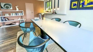 A modern dining area with a long table, blue chairs, a bookshelf, and a painting on the wall. - Ferienbungalow Iwele (Marktbreit)
