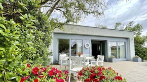 A modern building with a patio area featuring white furniture and potted red flowers. - Ferienbungalow Iwele (Marktbreit)