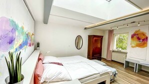 A modern bedroom with a skylight, a bed, a bedside table, a potted plant, and abstract wall art. - Ferienbungalow Iwele (Marktbreit)