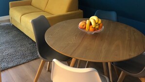 A room with a yellow sofa, a round wooden table with a fruit bowl, and a floor lamp. - Appartement Indépendant - Wifi - Parking- Petit Déjeuner (Ittenheim)