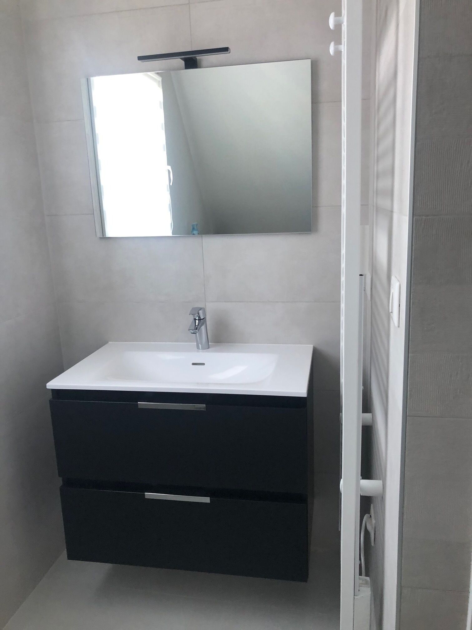 Une salle de bain avec un lavabo blanc, un meuble-lavabo noir et un miroir au-dessus.