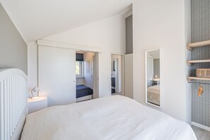 A modern bedroom with a large bed, a bedside table with a lamp, a wardrobe, and a mirror. - BADEBUDE 2 - Hampton-style vacation home near Weißenhäuser Strand, Baltic Sea (Oldenburg in Holstein)