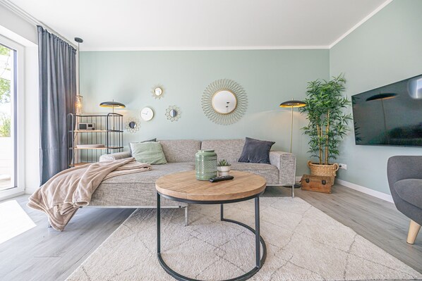 Un salon avec un canapé, une table basse ronde, un téléviseur et une plante.