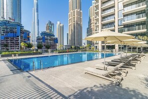 Una piscina con sillones de playa y sombrillas, rodeada de edificios altos.