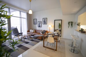 Un salon moderne avec un canapé, une table basse et une table à manger. On y trouve une grande fenêtre avec des rideaux, une plante et des tableaux encadrés accrochés au mur.