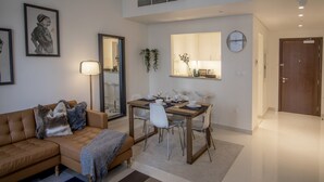 Een moderne woonkamer met een bank, een eettafel voor vier personen en een zichtbare keuken door een open deur.