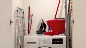 Een wasruimte met een voorlader wasmachine, een droogrek, een rode dweil en een rode emmer.