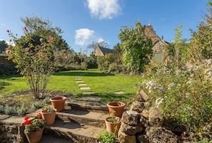 Stroll through the lush garden, surrounded by vibrant flowers and a traditional stone house with a thatched roof.