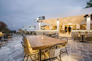An outdoor dining area with stone flooring, wooden tables, and wicker chairs. - Ladikos Garden (Rhodes)