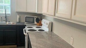 Una cocina con armarios blancos, microondas, estufa y encimera de granito.