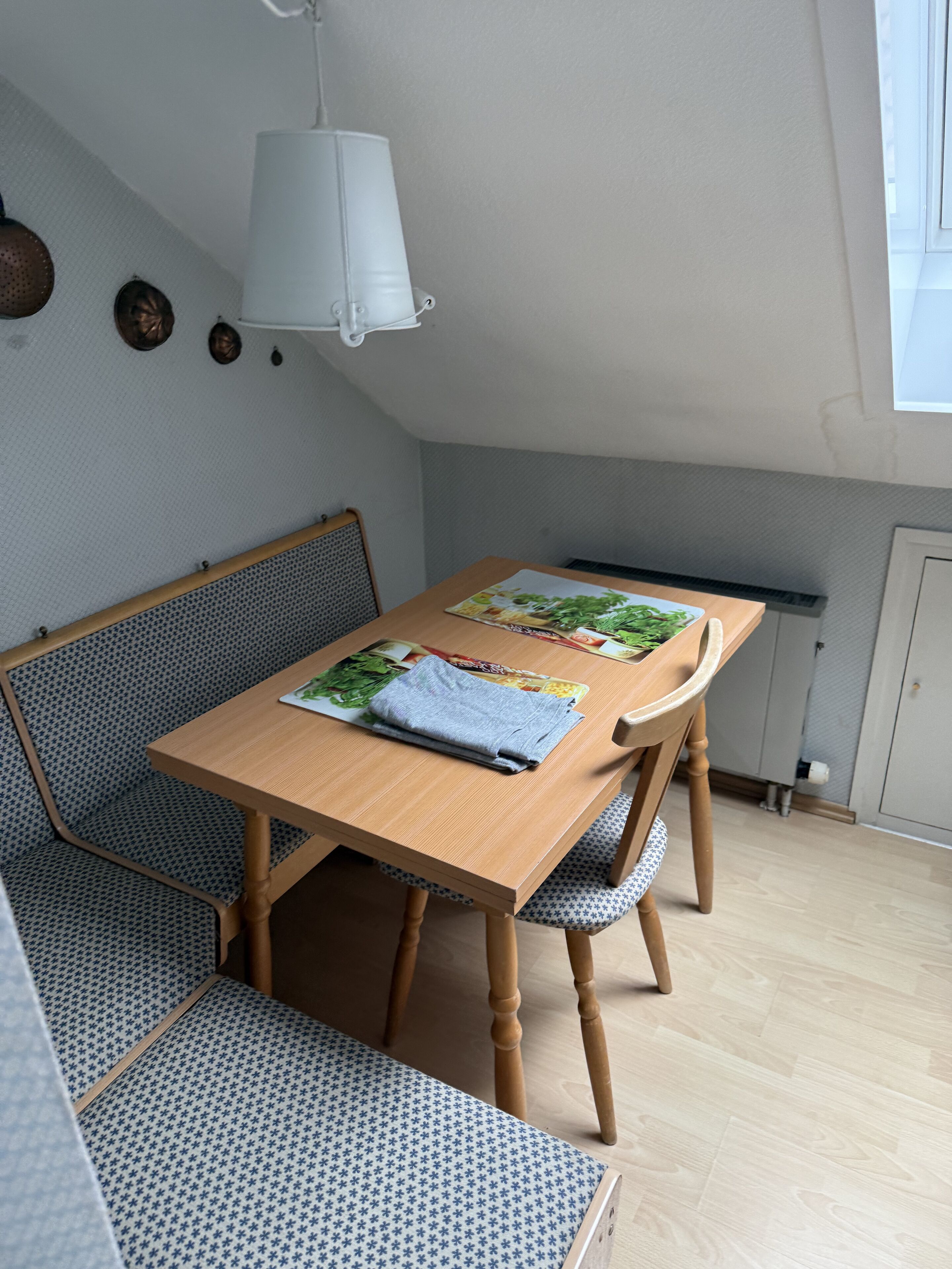 Un comedor con una mesa de madera, un banco azul estampada y una lámpara colgante blanca.