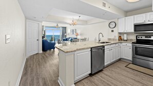 A modern kitchen with white cabinetry, a built-in dishwasher, stainless steel appliances, and a large island with a granite countertop. - Grande Atlantic 807 - 4 Bedroom Oceanfront Unit (Myrtle Beach)