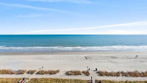 A beach with a clear sky, calm sea, and a few people walking. - Grande Atlantic 807 - 4 Bedroom Oceanfront Unit (Myrtle Beach)
