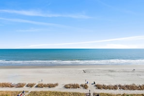 Una spiaggia con cielo sereno, mare calmo e alcune persone che passeggiano.