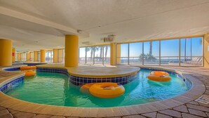 An indoor swimming pool with multiple lanes, yellow pillars, and clear views of the beach through large windows. - Grande Atlantic 807 - 4 Bedroom Oceanfront Unit (Myrtle Beach)