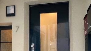 Eine schwarze Tür mit einem Glasfenster, einem Zifferncode-Schloss und einer kleinen Überwachungskamera darüber.