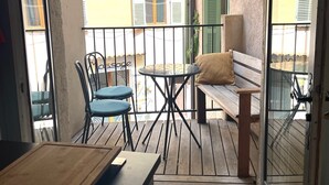 A balcony with a wooden table, two chairs, a bench, and a glass door. - Cozy studio with terrace in the heart of Old Antibes (Antibes)