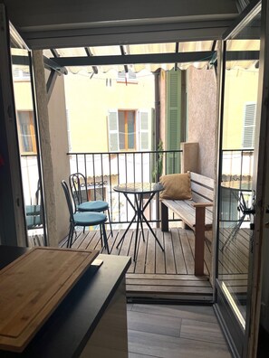 Ein Balkon mit einem Holztisch, zwei Stühlen, einer Bank und einer Glastür.