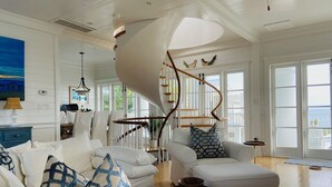 A spacious living room with a white sofa, patterned pillows, a wooden coffee table, and a spiral staircase leading to an upper level. - Gorgeous Listing in Seaside Proper with Beautiful Unobstructed Gulf Views (Santa Rosa Beach)