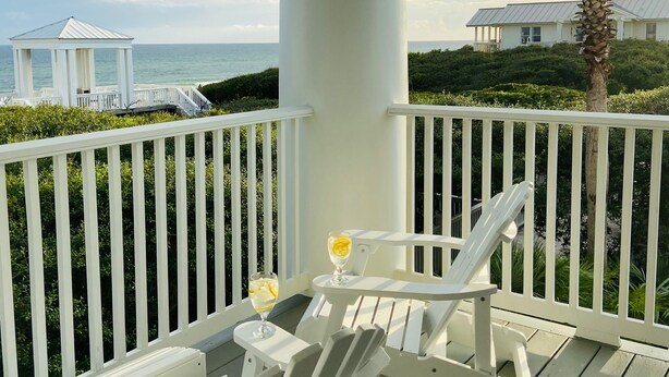 A covered outdoor area with white railings, two Adirondack chairs, and a glass of drink on the deck. - Gorgeous Listing in Seaside Proper with Beautiful Unobstructed Gulf Views (Santa Rosa Beach)