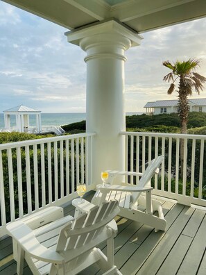 A covered outdoor area with white railings, two Adirondack chairs, and a glass of drink on the deck.