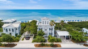 A coastal property with a large white building, a covered parking area, and a beach with blue umbrellas. - Gorgeous Listing in Seaside Proper with Beautiful Unobstructed Gulf Views (Santa Rosa Beach)