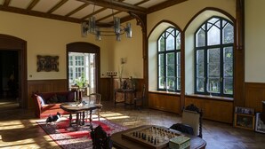 Una habitación amplia con suelo de madera, un sofá rojo, una mesa de ajedrez y grandes ventanales abovedados.