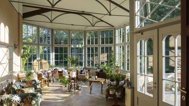 Un conservatorio iluminado por el sol, con techos altos, ventanas amplias y una variedad de asientos y plantas.
