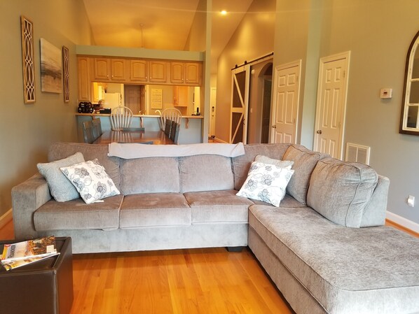 A living room with a grey sectional sofa, wooden flooring, and a kitchen in the background. - 3 Master Suite, 3 BA spacious townhome on SML with Boat and Slip (Huddleston)