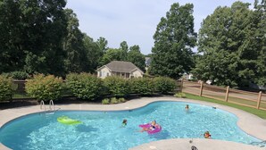 Una piscina con bordo curvo, una scaletta e alcune persone in acqua. Sulla banchina ci sono sedie a sdraio e un tavolo.