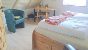 Un dormitorio con techo inclinado, una cama con ropa de cama blanca, un escritorio de madera y una silla.