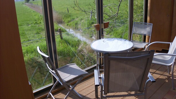 Una terraza con una mesa y sillas de vidrio con vista a un campo cubierto de césped.