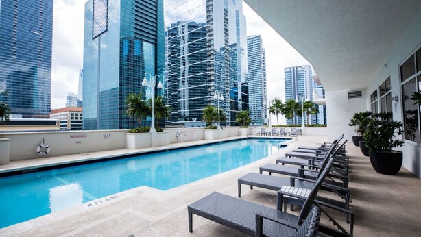 A rooftop pool with lounge chairs and palm trees, surrounded by high-rise buildings. - Amazing 2BR APT @Brickell, Free Parking (Miami)