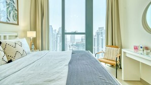Habitación de hotel con una cama grande, un escritorio, una silla y vistas a la ciudad a través de amplios ventanales.