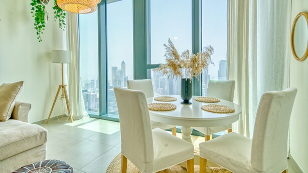 Un comedor moderno con una mesa redonda, sillas blancas y vistas a un paisaje urbano a través de amplios ventanales.