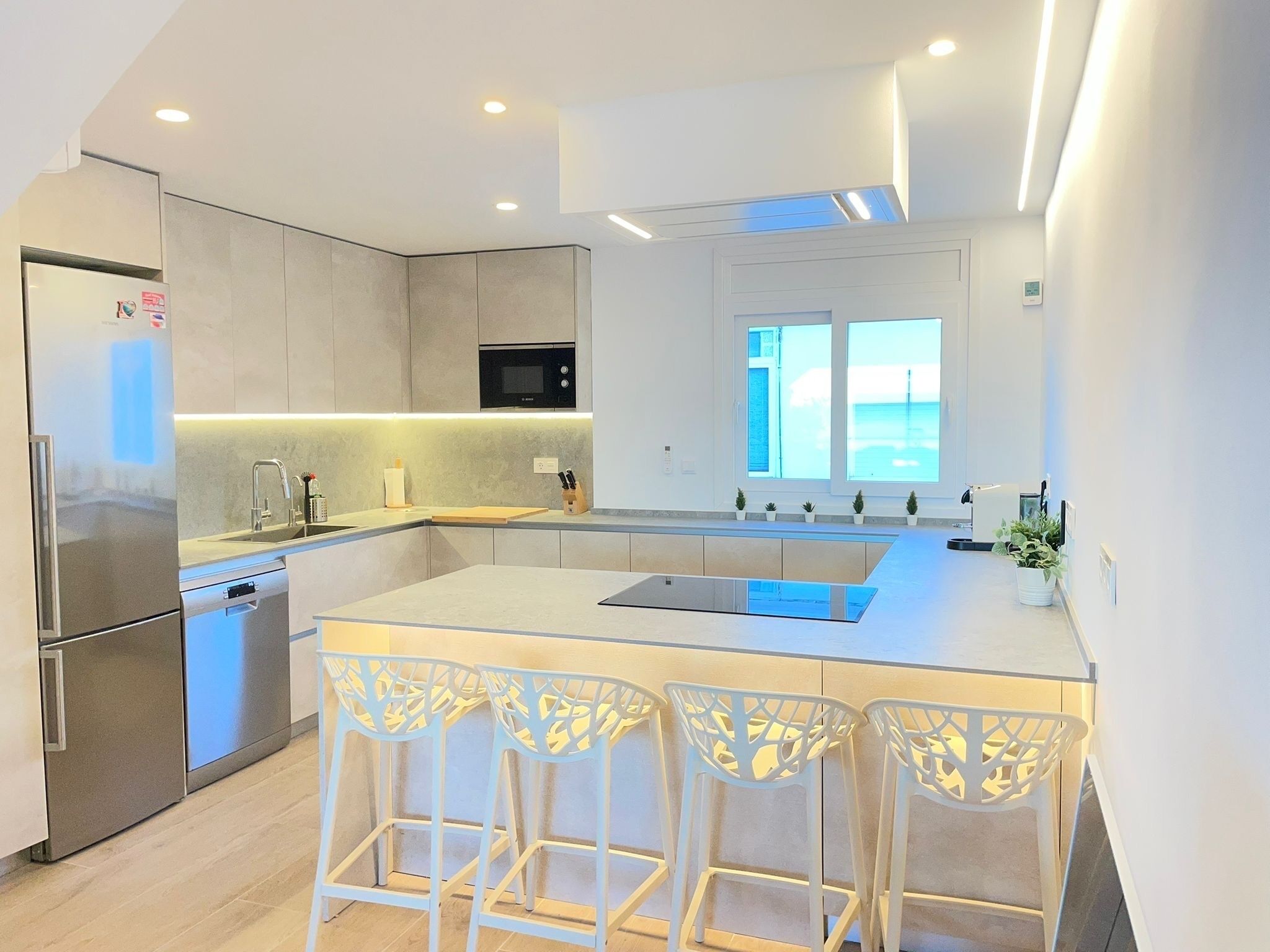 Een moderne keuken met een centraal eiland, barstoelen, een ingebouwde oven en een raam met uitzicht.