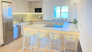 A modern kitchen with a central island, bar stools, a built-in oven, and a window providing a view. - Just 5 Steps to the Beach · Stylish Whole House · AC · Terrace & BBQ · WIFI (Cunit)
