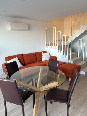 A modern living room with a glass-top coffee table, a red sofa, and a staircase with white railings.