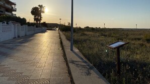 A paved walkway with patterned tiles, a street lamp, and a grassy field with a signboard. - Just 5 Steps to the Beach · Stylish Whole House · AC · Terrace & BBQ · WIFI (Cunit)