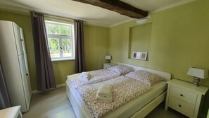 Un dormitorio con cama, mesitas de noche, armario y ventana con cortinas.