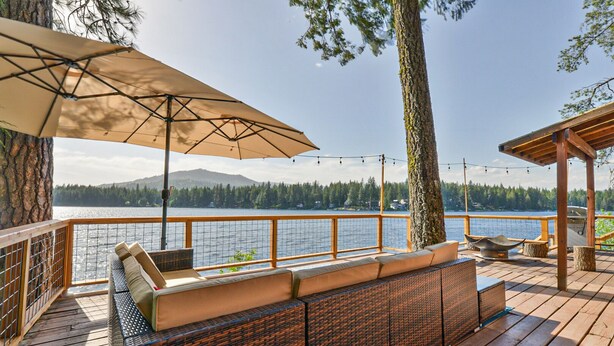 Um deck de madeira com mobiliário externo, uma pérgola e vista para um lago.