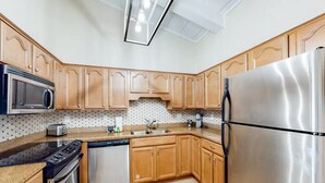 A modern kitchen with wooden cabinets, stainless steel appliances, and a patterned backsplash. - 300 Steps to the Emerald Beach (Destin)
