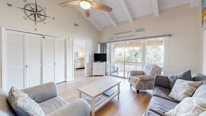 A spacious living room with a ceiling fan, a large window, and a TV. - 300 Steps to the Emerald Beach (Destin)