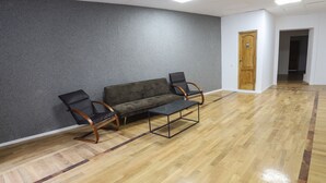 Une pièce avec un mur gris à texture, un plancher en bois, un canapé, deux fauteuils et une porte.