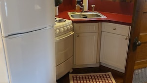 Une cuisine de taille réduite avec un réfrigérateur, une cuisinière et un évier blancs. On y trouve des meubles de cuisine en bois et une fenêtre avec des rideaux.