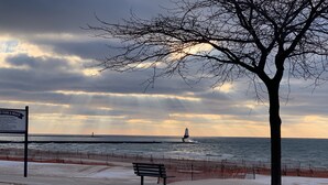 Un banc et un panneau près d’une plage, avec un phare visible au loin.