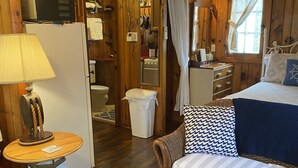 Une chambre confortable, aménagée dans le style d’un chalet, avec un lit, une petite table et une lampe, un fauteuil en osier et un plancher en bois.