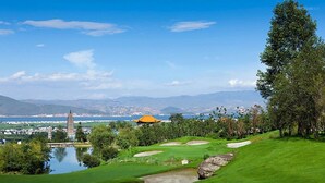 Um campo de golfe com um lago, árvores e uma vista distante de montanhas e edifícios.