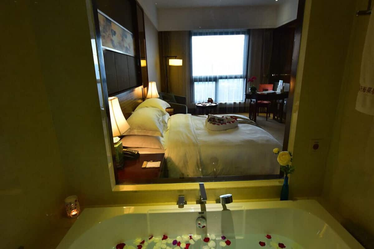 A hotel room with a large bed, a sitting area with a table and chairs, and a bathtub filled with rose petals.